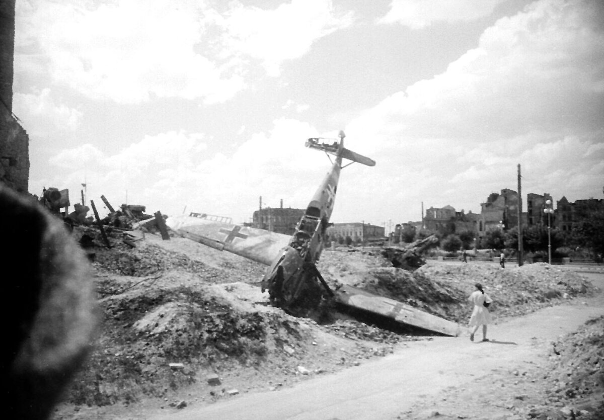 Подбитый и севший на вынужденную (у самолета выпущены шасси) немецкий истребитель Мессершмитт Bf.109 в центре Сталинграда. Лето 1943 года.