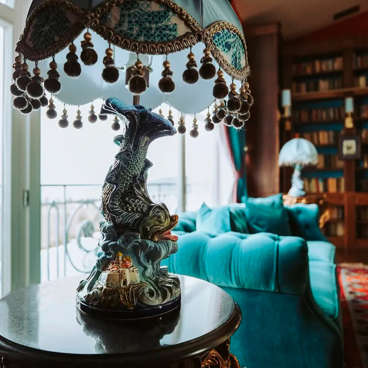 Настольная лампа «Морское царство» бренда «Романов Фаянс» — это многомерная композиция: завитки морской пучины, нависающие над крепостью и грозящие своей мощью кораблю. Фигура рыбы с еле уловимыми движениями ажурных плавников и игрой света на мельчайших чешуйках. И во главе композиции — абажур с мягкими кисточками, тень от которых наполняет пространство. Одно нажатие выключателя оживляет подводное царство, замершее в этои  композиции, добавляя еще  больше волшебного сияния. Благодаря форме абажура свет мягко рассеивается по комнате. Такая лампа станет отличным украшением туалетного столика или комода для создания камерного освещения. Вы можете приобрести лампу без абажура, либо его можно изготовить по вашему индивидуальному заказу.