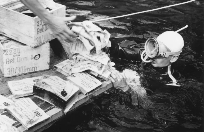 Аквалангист передает поддельные нацистские записки с озера Топлиц в Австрийских Альпах в 1959 году. Банкноты были подделаны нацистами во время Второй мировой войны в попытке дестабилизировать британскую экономику, но в конце войны были сброшены в озеро. 
Keystone/Getty Images