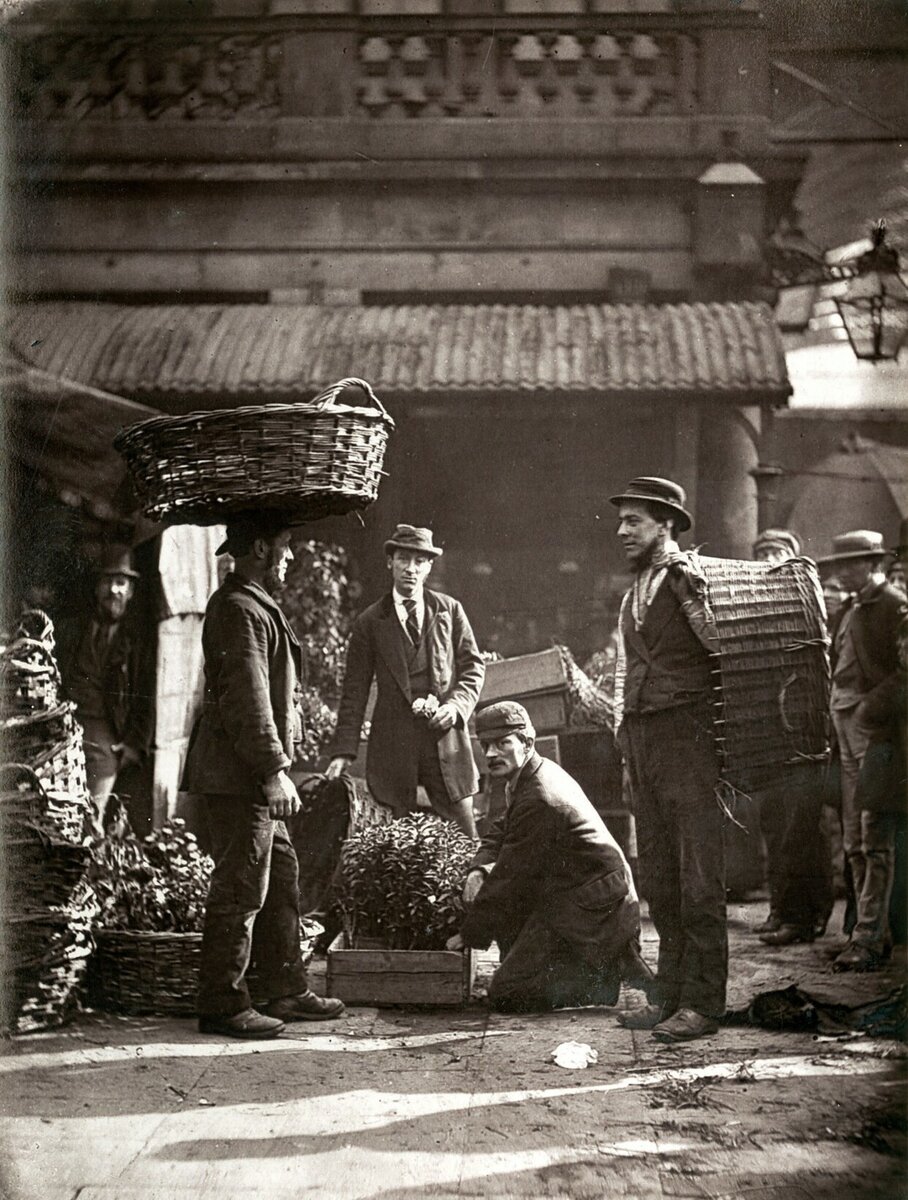 Эта коллекция фотографий 1873-1877 годов входит в книгу «Уличная жизнь в Лондоне», которая была одним из первых экспериментов в жанре социальной документальной фотографии. Авторы книги, фотограф Джон Томсон и журналист Адольф Смит, с помощью фотографий и очерков хотели показать, в каких условиях живут бедняки в Лондоне.
Мужчины на фото - рабочие на службе у мистера Диксона, известного флориста. Их бизнес строго ограничен цветами, и они не занимаются ни овощами, ни фруктами. Больше сотни цветочных киосков на оптовом цветочном рынке ждут, когда они доставят к ним свежий товар, и, по грубым подсчетам, две тысячи человек заняты тем, что выращивают и привозят цветы для продажи на этих лотках, а еще две тысячи человек заняты разноской различных партий цветов множеству постоянных покупателей. Именно этих разносчиков и можно увидеть в Ковент-​Гардене ранним утром, когда они собираются в одном месте, чтобы получить задание на сегодня и вскоре рассеются по всем районам мегаполиса, нагруженные растениями всех видов. На фото лишь малая часть доставщиков цветов на дом, но скоро разойдутся и они.
