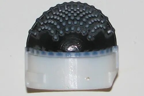 Прорези на тактильной коже, напечатанной на 3D-принтере. Белый пластик является жестким креплением для гибкой черной резиновой кожи. Обе части сделаны вместе на продвинутом 3D-принтере. Штифты на внутренней стороне кожи повторяют дермальные сосочки, которые формируются внутри кожи человека.