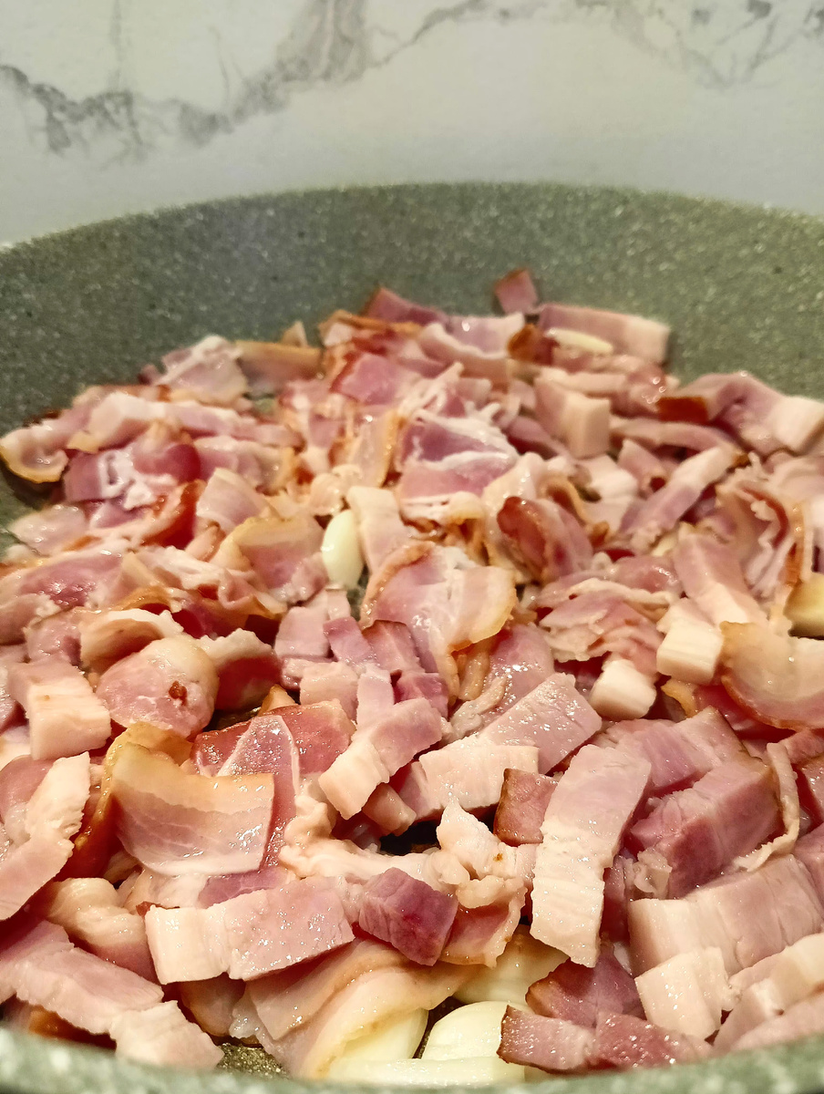 Чеснок нарезаем на большие кусочки, надавливаем на него ножом, чтобы выступил сок и отправляем к бекону, обжариваем все вместе до золотистости 