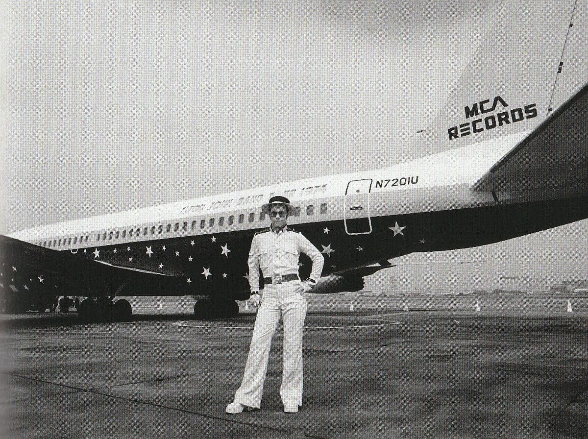 Как на подиуме: на фоне самолёта "Старшип", перекрашенного в соответствии с пожеланиями артиста. Отголосок звездной футболке с легендарного концерта в "Трубадуре" (первые гастроли в США).