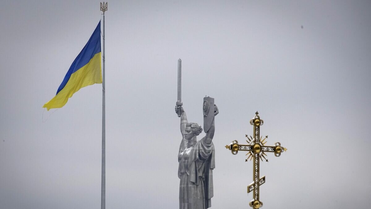    Крест монастырского комплекса Печерской Лавры на фоне украинского государственного флага и монумента Родина-мать в Киеве© AP Photo / Efrem Lukatsky