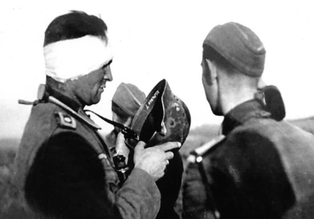 Немецкий солдат осматривает свой шлем после попадания.