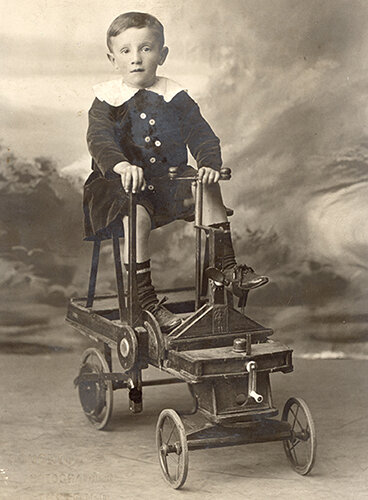 Фотография 1917 года из коллекции Веломузея Андрея Мятиева, запечатлевшая ребенка на игрушечном автомобиле с ручным приводом.