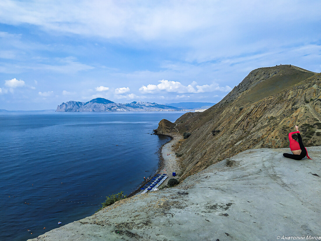 На краю обрыва сидела девушка в красной футболке и демонстрировала свою гибкость.