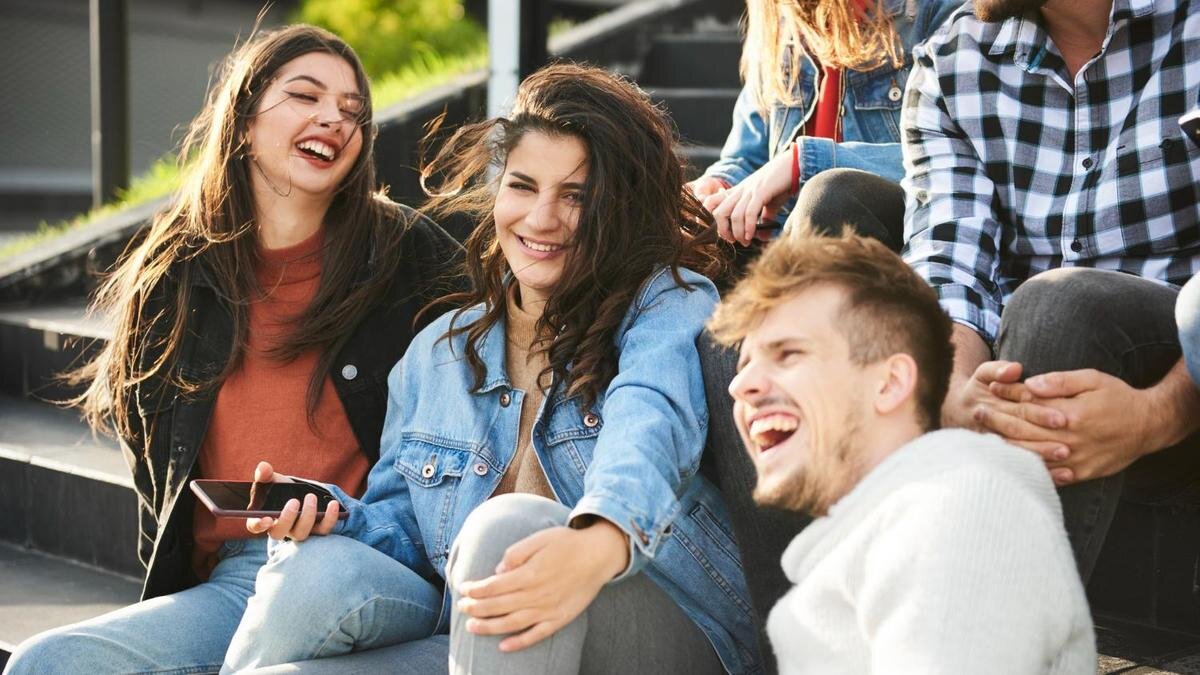    Компания молодых людей сидит на ступеньках. Парень и девушки смеются:Freepik