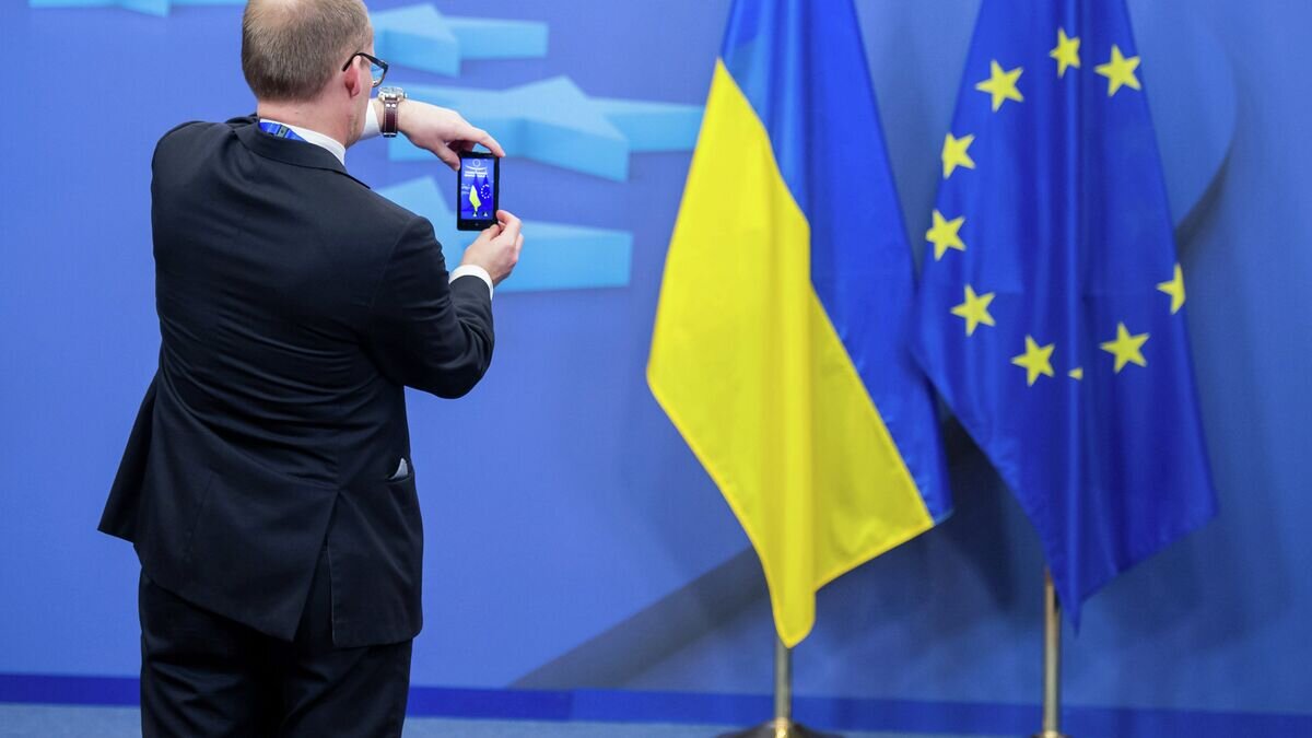    Человек фотографирует флаги Украины и Евросоюза© AP Photo / Geert Vanden Wijngaert