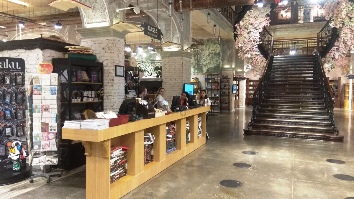 Первый этаж. Входная группа магазина. Слева - стойка продавцов-консультантов. Напротив входа расположена кованая лестница, ведущая на верхний этаж. Она украшена хорошо сделанными гирляндами из искусственных цветов. Всего этажей - два и еще ярус второго этажа. Нас ждет сказка в трех частях. Атмосфера завораживает. Это всё, что хотите, только не книжный магазин, вообще не магазин. Музей, разместившийся в замке барона из средневековья. Листайте галерею первого этажа, почувствуйте пространство и вкус дизайнера.