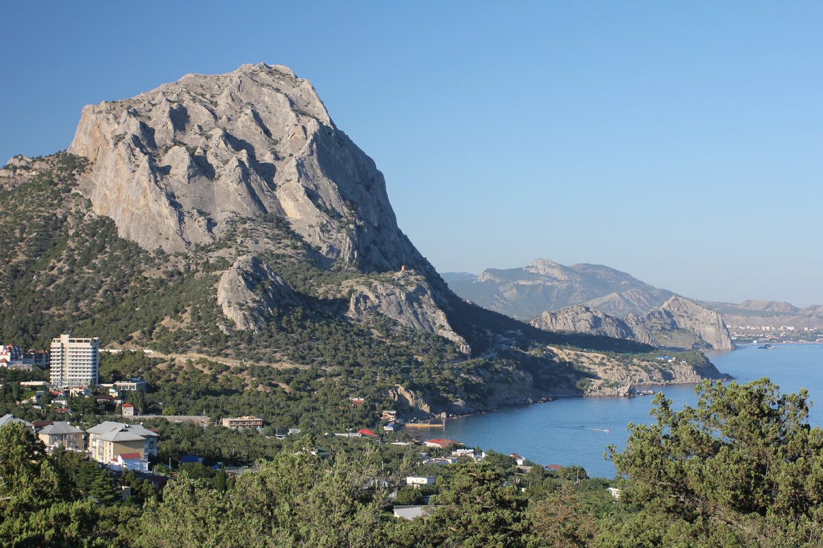 Гора Сокол. Древний рифовый массив. Вдали можно разглядеть город Судак и рифовую скалу, на которой расположилась генуэзская крепость. На переднем плане поселок Новый Свет. У подножия Сокола видна единственная дорога в поселок.