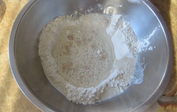 В первую очередь проверяем и активизируем дрожжи. Делаем быструю опару. В муку (в углубление) вливаем тёплую воду, засыпаем сахар и дрожжи. Слегка перемешиваем, добавляя чуть-чуть муки, и даем постоять опаре минут 20 (можно накрыть полотенцем или плёнкой).