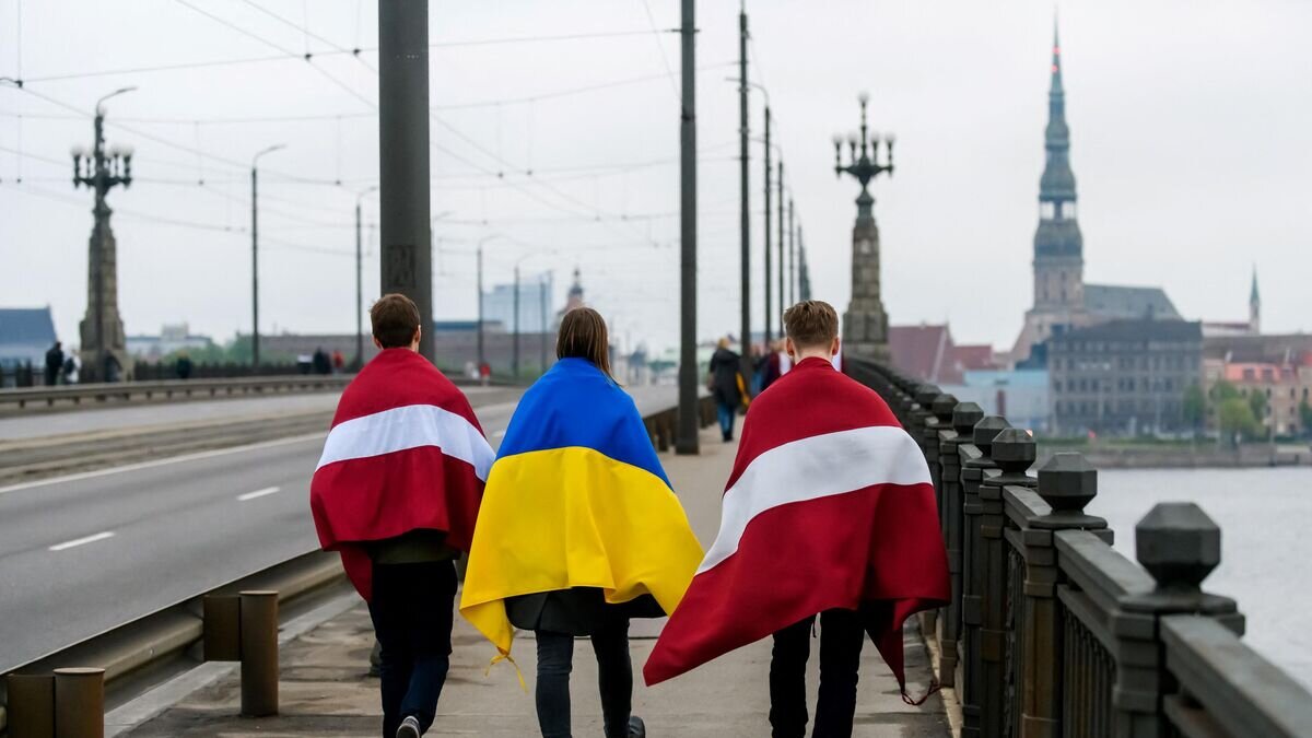    Молодые люди с флагами Латвии и Украины на плечах в Риге © AFP 2022 / Gints Ivuskans