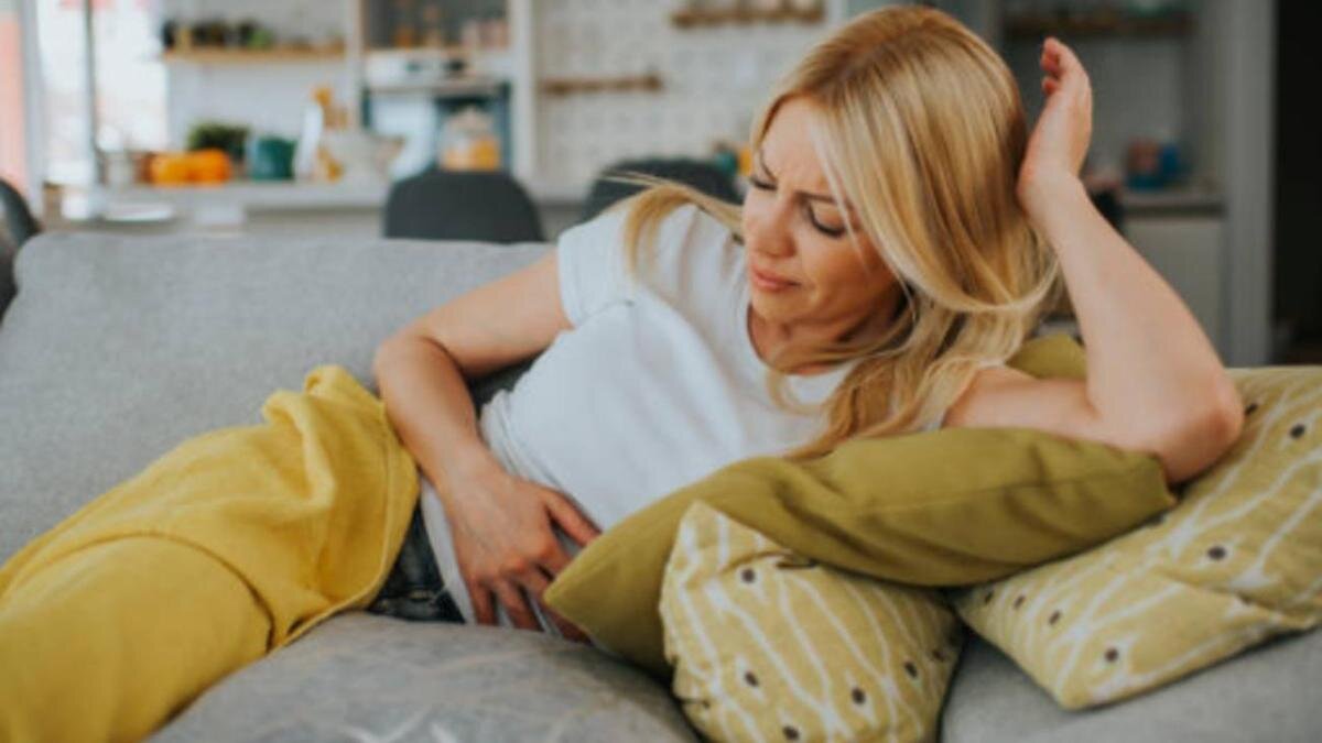    Женщина лежит на диване и держит руку на животе:iStockPhoto