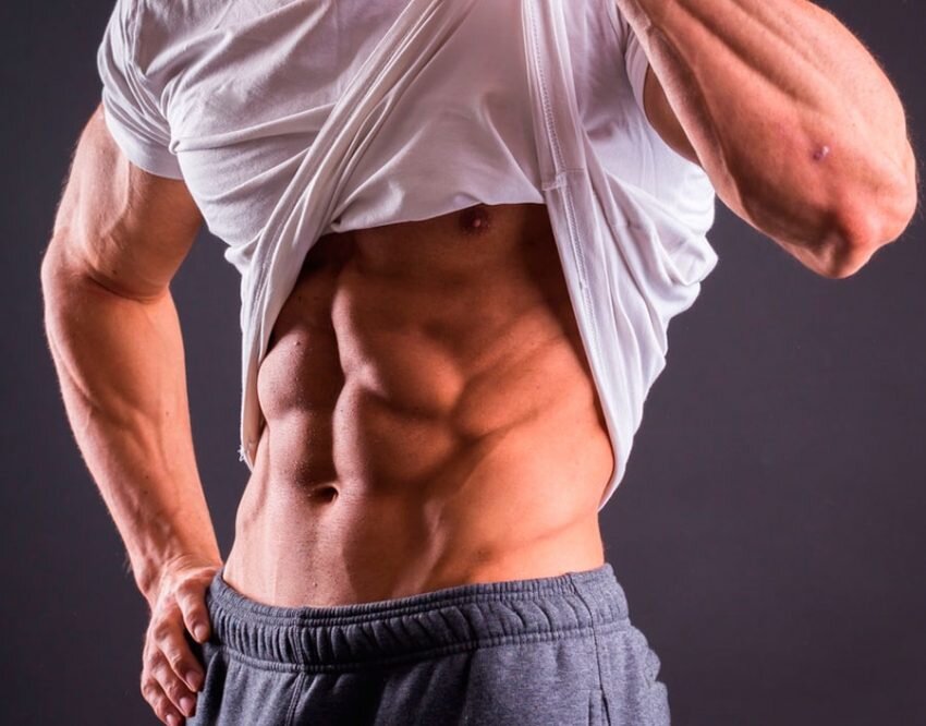 КАК БЫСТРО НАКАЧАТЬ ПРЕСС. СОВЕТЫ МУЖЧИНАМ

Во все времена показателем мужской силы и подтянутости считались не только мышцы рук и плеч, но и накачанный пресс. Практика различных тренировок показывает, что область живота — одна из самых трудных для проработки мышц. Но если выполнять упражнения комплексно и регулярно, то видимые результаты не заставят себя ждать.

Как накачать пресс в зале
ОСОБЕННОСТИ ТРЕНИРОВОК ДЛЯ ПРЕССА

Обычно у парней пресс развит намного меньше, чем другие группы мышц — это связано со скоростью реакции на тренировки. В среднем, сроки прокачки следующие:

Плечевая область и руки — 15 дней после начала тренировки.
Область груди и спины — 20-25 дней.
Область бедра, мышц таза и голени — 20-30 дней.
А вот мышцы пресса не только сложны в проработке, но и скрыты под защитной жировой прослойкой. Чтобы увидеть первые признаки окрепшего пресса, придется поработать не меньше 40 дней. Кроме того, мышцы живота имеют несколько слоев волокон, которые расположены в разных направлениях: внутренние, внешние, прямые и поперечные. Поэтому для пресса необходимо выполнять целый комплекс разнонаправленных тренировок: упражнения на наклонной скамье, скручивания, подъем ног, планку и т.д.

Еще одна важная особенность — мышцы в области живота восстанавливаются гораздо быстрее, чем остальные. Это связано с тем, что пресс почти круглосуточно находится в работе, помогая не только удерживать тело в прямом положении, но и поддерживать внутренние органы. Продолжительный отдых между тренировками в случае с прессом не принесет хороших результатов.

Многим известно правило, что мышцы растут именно в период отдыха, поэтому необходимо давать им достаточно времени на восстановление. Обычно каждую группу мышц прорабатывают по схеме: 1 день тренировок и 2 дня отдыха. Пресс можно загружать гораздо чаще. Многие тренеры советуют делать это ежедневно, но лучше все же придерживаться более мягкой схемы — день тренировок и день отдыха.

Это позволяет достичь сразу нескольких целей:

Мышцы успевают восстановиться, а значит их рост будет проходить быстрее.
Можно интенсивно увеличивать количество упражнений и подходов без риска перенапряжения и срыва.
Эффект от тренировок накапливается, а значит достижение цели ускоряется.
Обычно тренировки для пресса разделяют на две группы: упражнения на верхний пресс и нижний. Оба отдела можно прорабатывать как дома, так и в зале. Однако в тренажерном зале под наблюдением тренера это сделать намного проще.

КАЧАЕМ ВЕРХНИЕ МЫШЦЫ

Для мышц верхнего пресса самым эффективным упражнением считается скручивание. От классического жима на пресс, который все мы делали в школе, скручивание отличается тем, что от пола отрываются только лопатки и верхняя часть спины, а поясница и тазовая часть остаются плотно прижатыми к полу.

Накачать верхние мышцы пресса мужчине
ПРЯМЫЕ СКРУЧИВАНИЯ

Это упражнение отлично подойдет для начального уровня. Исходное положение — лежа прямо на полу, ноги согнуты в коленях, ступни плотно прижаты к полу, руки в замке за головой. Чтобы немного упростить упражнение, можно зацепиться ступнями за устойчивую мебель, например, положить их под шкаф или низкий диван. Так нагрузка с мышц живота частично распределяется на ноги.

Начинаем поднимать верхнюю часть спины, но следим за тем, чтобы поясница оставалась на полу. Лучше всего начать с 15-20 повторений по 2-3 подхода.

СКРУЧИВАНИЕ С ПОДЪЕМОМ НОГ

Если предыдущее упражнение кажется слишком простым, то можно усложнить его с помощью подъема ног. Упражнение проделывается в том же порядке, только ноги, согнутые в коленях, нужно приподнять над полом на 15-20 см и зафиксировать в неподвижном положении.

Еще более сложный вариант тренировки — делать скручивание с одновременным подъемом ног, согнутых в коленях. Причем в исходном положении ступни должны быть прижаты к полу, а при скручивании колени нужно как можно ближе притягивать к голове.

ВЕЛОСИПЕД

Это упражнение позволит качать не только прямые, но и косые мышцы пресса. Исходное положение: лежа на спине, колени согнуты и слегка приподняты над полом, руки в замке над головой. Поднимая верхнюю часть спины, попеременно поворачивайтесь вбок левой и правой стороной, поднимая противоположное колено. Цель упражнения в том, чтобы как можно ближе подтянуть локти к коленям и задержаться в таком положении на одну-две секунды.

Любое из перечисленных упражнений можно усовершенствовать с помощью вертикальной скамьи для тренировок — она удобная и функциональная. Лучше приобрести специальную спортивную скамейку для домашних занятий, чтобы иметь возможность регулировать угол наклона.

КАЧАЕМ НИЖНИЙ ПРЕСС

Если для проработки верхней брюшной части нужно поднимать грудную область, то для проработки нижней части нужно поднимать ноги. Лучше всего выполнять это упражнение не на полу, а используя длинную скамью.

Накачать нижние мышцы пресса мужчине
ПОДЪЕМ НОГ

Это эффективное упражнение для накачивания мышц пресса можно выполнять на разных уровнях сложности. Исходное положение: лежа на спине, ноги согнуты в коленях, а руки лежат вдоль туловища ладонями вниз. Поднимаем обе ноги так, чтобы поясница приподнималась над полом, а лопатки оставались плотно к нему прижаты.

Для более подготовленных подойдет упражнение с прямыми ногами. Поднимать их следует примерно на 45 градусов к полу. Если трудно поднимать ноги, можно взяться руками за боковушки скамьи.

ВЕРХНЕЕ СКРУЧИВАНИЕ

Помогает развить не только нижний пресс, но и косые мышцы живота. Исходное положение: прямые ноги подняты на 90 градусов к телу, поясница и лопатки плотно прижаты к полу, руки вдоль тела. Поочередно скручивайте обе ноги то в левую, то в правую стороны. Следите за тем, чтобы таз как можно меньше отрывался от горизонтальной поверхности.

Это упражнение также удобно выполнять на скамье, чтобы придерживаться руками во время скручивания тела.

ПЛАНКА

Это универсальное упражнение, которое позволяет накачиваться не только мышцам пресса, но и мышцам спины, рук и плеч. Исходное положение как при отжимании: на вытянутых руках, упираясь в пол, тело прямое, поясница не прогибается вниз, ноги сведены вместе. Пресс и ягодицы напряжены. Держать такое положение следует не менее 30 секунд.

Упростить планку можно, опираясь на локти, а усложнить — с помощью подъема и удержания одной из ног. Также можно делать боковую планку, когда опора осуществляется только на одну руку, а таз расположен параллельно полу. Вторую руку можно вытянуть вверх или заложить за голову.

УПРАЖНЕНИЯ ДЛЯ ПРЕССА В ЗАЛЕ

ИСПОЛЬЗОВАНИЕ УТЯЖЕЛИТЕЛЕЙ

Чтобы увеличить нагрузку на пресс, тренеры советуют использовать утяжеления. Лучше всего для этого подойдут блины от штанги. Их удобно держать в руках, а вес распределяется строго параллельно телу.

Во время скручиваний вес обычно удерживается обеими руками на груди. Следует крепко прижать блин к груди, держа руки крест-накрест. Еще один способ — зафиксировать вес руками за головой, но такой метод опасен, хоть и увеличивает сопротивление.

УПРАЖНЕНИЯ НА НАКЛОННОЙ СКАМЬЕ

В зале существуют специальные скамейки для пресса, с валиком для поддержания ступней или бедер. На них возможно выполнение любого из вышеописанных упражнений как с отягощением, так и без него. Важно помнить, что чем больше вертикальный наклон скамьи, тем труднее выполняется упражнение.

Кроме описанных выше упражнений эффективно использовать скамью для бокового пресса. Для этого нужно опуститься на наклонную (примерно 45 градусов) скамью боком так, чтобы упираться ногами в пол. При этом верхняя часть тела должна располагаться свободно. Выполняем боковые скручивания так, чтобы не только опускаться вниз на вдохе, но и подниматься максимально вверх от исходного положения.

ИСПОЛЬЗОВАНИЕ ТРЕНАЖЕРОВ

Функциональные тренажеры, которыми снабжаются залы, полезны тем, что позволяют нагрузить любые группы мышц. Разнообразие упражнений дает возможность избавится от «эффекта привыкания», когда тело перестает положительно реагировать на одно и то же упражнение. Эффективно выполнять скручивания сидя и лежа, используя тягу на блоках-роликах. Они помогают правильно распределить усилия и подобрать нужный вес для каждого упражнения.

Упражнения для пресса в зале
РАСПРОСТРАНЕННЫЕ ОШИБКИ

Вот несколько ошибок, которые совершают даже опытные спортсмены при прокачке мышц пресса:

Неправильное выполнение. Большинство из тех, кто занимается без контроля тренера, пренебрегают техникой выполнения упражнений.Помните: лучше сделать меньше упражнений, но выполнить их правильно.
Долгий отдых. Не стоит давать мышцам пресса длинную передышку, иначе будет сложно войти в постоянный ритм, а каждое упражнение станет даваться все сложнее.
Отсутствие комплексных упражнений. Пресс — это не единственная мышца, которая обеспечивает нам видимые кубики. Мышцы спины и поясницы поддерживают спину ровной и также требуют хорошей проработки.
Нет развития тренировок. При достаточном отдыхе организм быстро привыкает к нагрузкам и требует постоянного усложнения программы и увеличения количества подходов и повторений.
Чрезмерное утяжеление. Не следует пренебрегать личной безопасностью, особенно используя подручные веса, ведь большая нагрузка на пресс и поясницу может привести к травмам.
ПРАВИЛЬНАЯ ДИЕТА ДЛЯ ИДЕАЛЬНОГО ПРЕССА

Чтобы не только усилить мышцы живота, но и создать притягательный для женского взгляда рельеф, одних упражнений недостаточно. Инструкторы фитнес-залов утверждают, что залог появления всех шести кубиков — это на 90% питание, и только на 10% — тренировки.

Такие цифры прямо указывают на то, что с неправильным питанием идеальный пресс может быть навечно погребен под слоем жира. Поэтому вот несколько советов для тех, кто хочет усилить результат тренировок:

Лучше всего разделить питание на 5-6 приемов пищи в день. При этом порции должны быть небольшими (примерно 1/3 от привычной нормы), а перерыв между приемами — не более 2-2,5 часов. Так тело будет всегда получать белок и углеводы, а жиры не успеют скопиться.
Основное меню должно содержать каши (гречневую, перловую, рисовую), нежирное мясо курицы, рыбу, бобовые, овощи и фрукты. От жареных, жирных, копченых, сладких и хлебобулочных продуктов лучше отказаться полностью.
Большое потребление воды — это условие для быстрого метаболизма. За день в организм должно поступать не менее 2 литров чистой воды.
Правильное соотношение белков, жиров и углеводов выглядит следующим образом — 50/20/30.
Ни в коем случае нельзя голодать, ведь при недостатке питания организм потребляет не столько жировую, сколько мышечную массу.
Чтобы как можно быстрее добиться красивого и рельефного пресса, нужно уделять внимание всему комплексу упражнений как верхнего, так и нижнего отдела, а также правильному питанию.