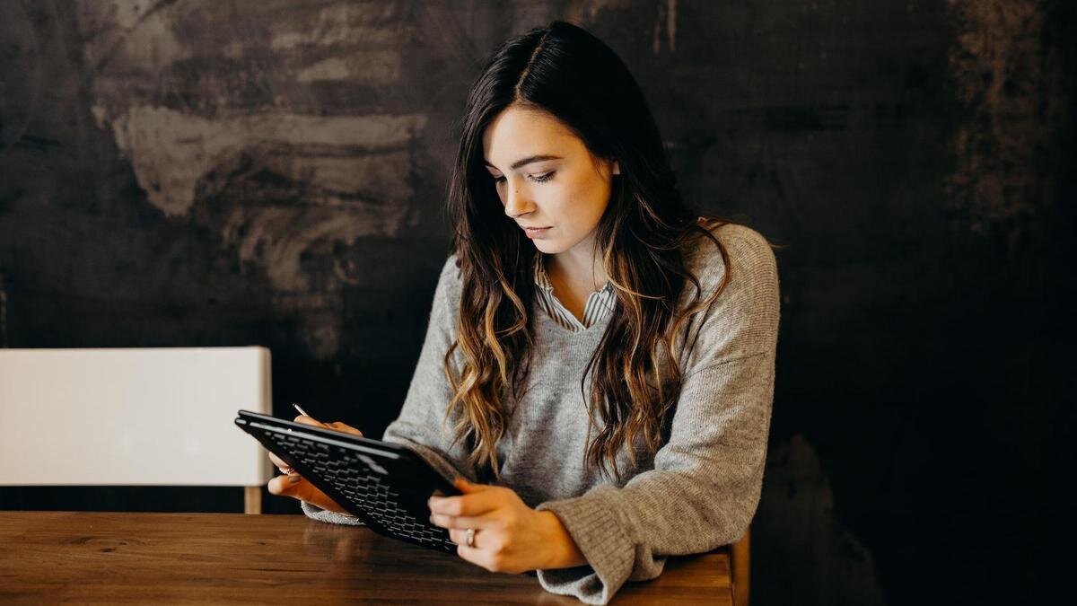    Девушка в сером платье сидит за столом и работает за планшетом:Unsplash/Brooke Cagle