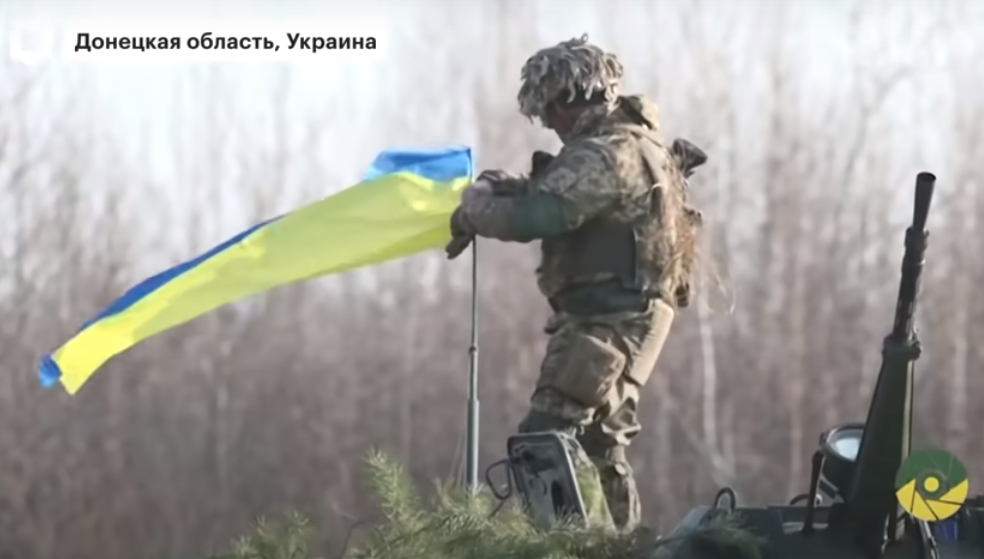 Солдат ВСУ крепит украинский флаг над башней бронемашины, которую перебрасывают к линии соприкосновения, на Донбасс. Скриншот из выпуска передачи канала "РБК"