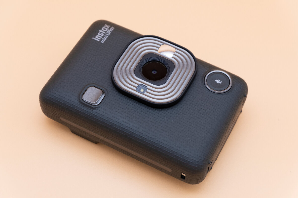 Instax mini LiPlay, вид спереди. На фото - объектив, кнопка спуска затвора и кнопка записи звука. Да, тут даже такое есть. Потом звук визуализируется на фотогрfфии в виде куар кода. Сам звук можно прослушать, если отсканировать код. Листайте дальше ->