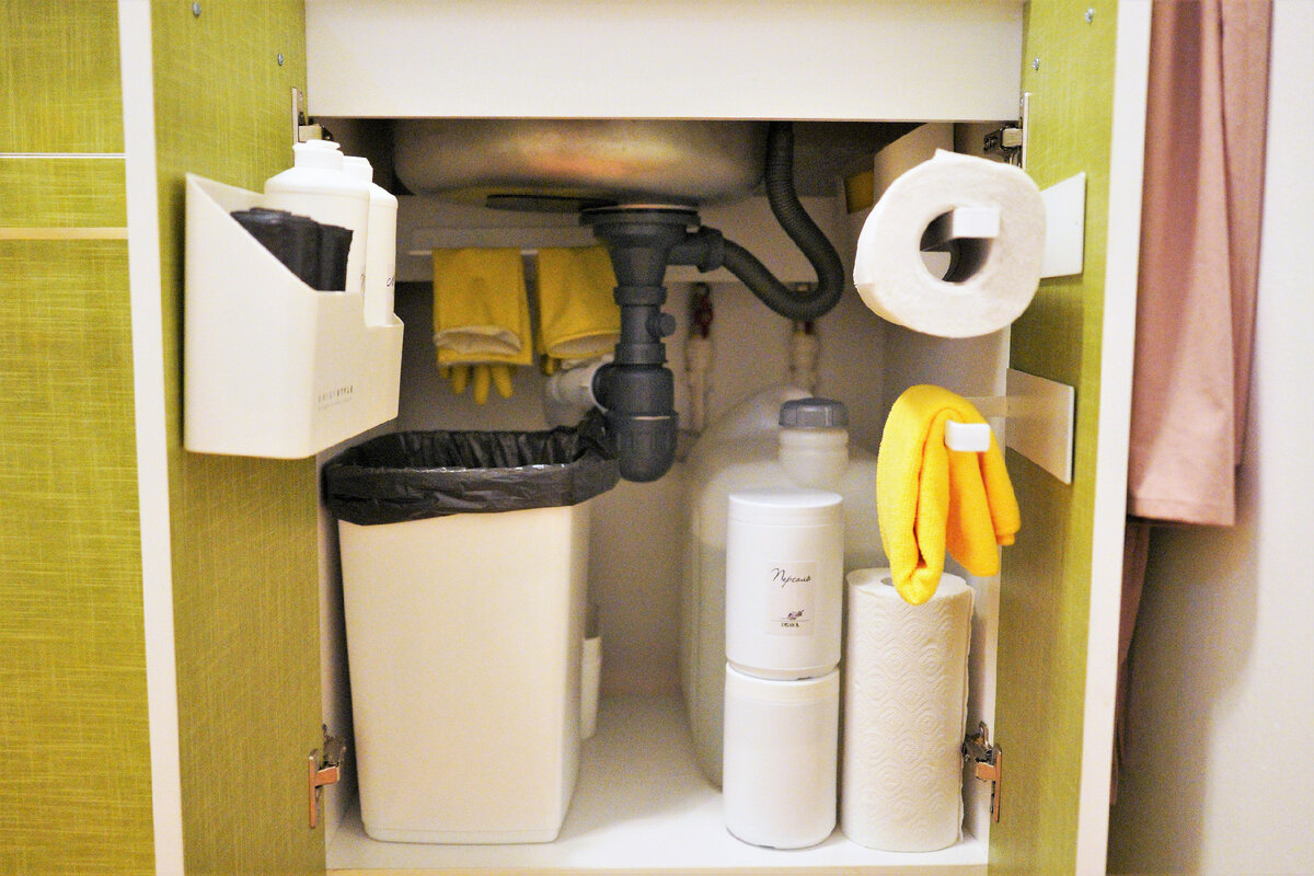 Обновленный шкафчик под мойкой. На дверках: пластиковый держатель для моющего средства и мусорных мешков, металлические держатели для бумажных полотенец и половой тряпки. В канистре - 15 литров воды. Впереди - запас персоли. Позади мусорного ведра - контейнер со всеми чистящими средствами. Листайте дальше.