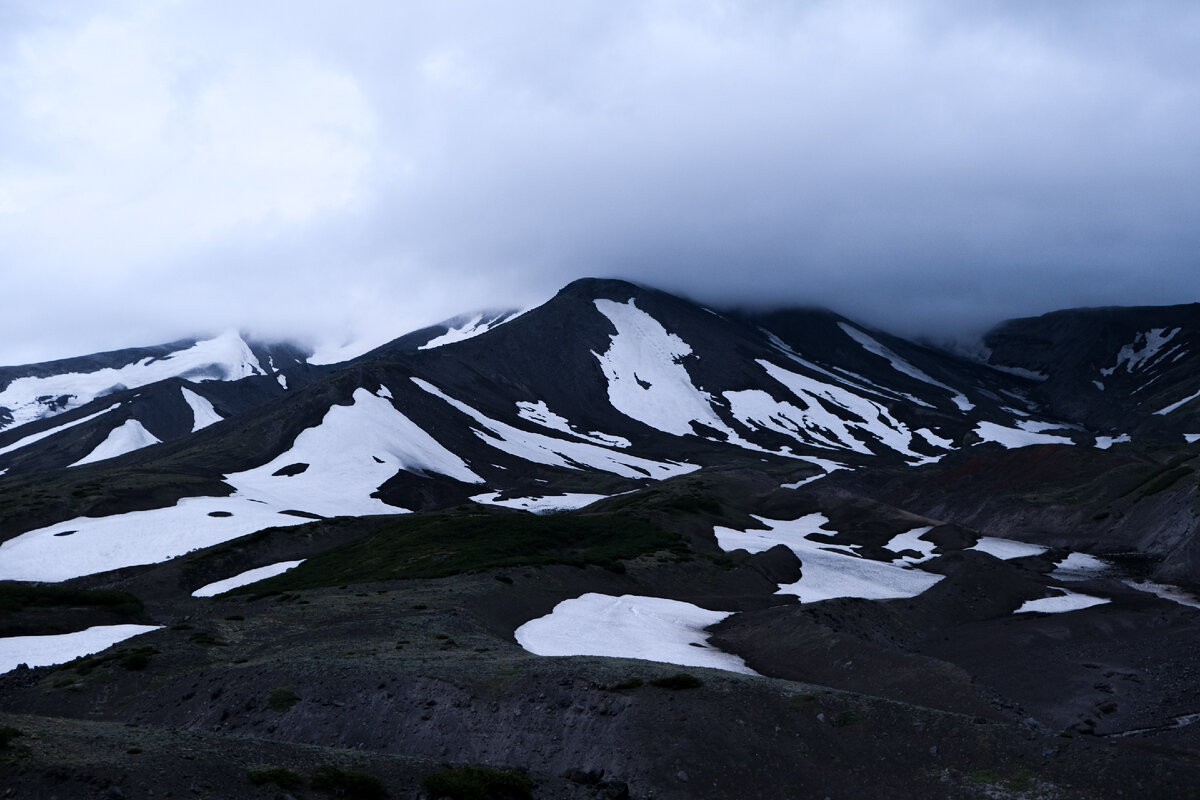 Нам предстояло четвертое восхождение в нашем туре на Камчатке. На это раз мы должны были покорять Авачинский вулкан(2741 метр) - самый близкий вулкан к Петропавловску. Он затесался между двумя другими вулканами Петропавловска - Корякским 3456 метров и Козельским 2189 метров. Это те три великана, которые чаще всего появляются на фотографиях с Камчатки, их хорошо видно с любых точек в Петропавловске. Несмотря на близость к цивилизации, добраться сюда не так просто. Дороги к основанию вулканов нет. Ехать можно только на высокопроходимых машинах. Местами приходиться проползать по руслу реки, которая весной бывает очень буйной. Условия спартанские, но самая жесть - это услуги душа. Он стоил 700 рублей. Даже в исландских кемпингах все это стоит в разы дешевле. Ночевали мы в небольших бытовках на 6-8 человек. Обычные шконки, на которых можно расстелить спальник и укутаться в нем.  