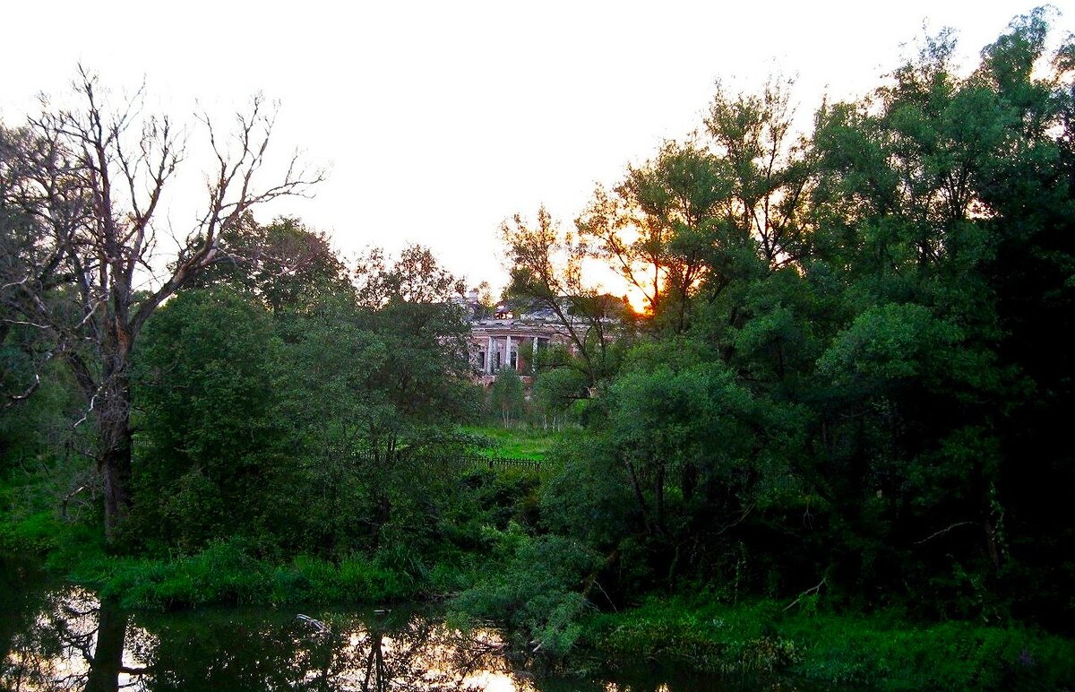 Сквозь зелень виднеется главный дом усадьбы. Вид с моста через речку Лопасню. Фото автора.