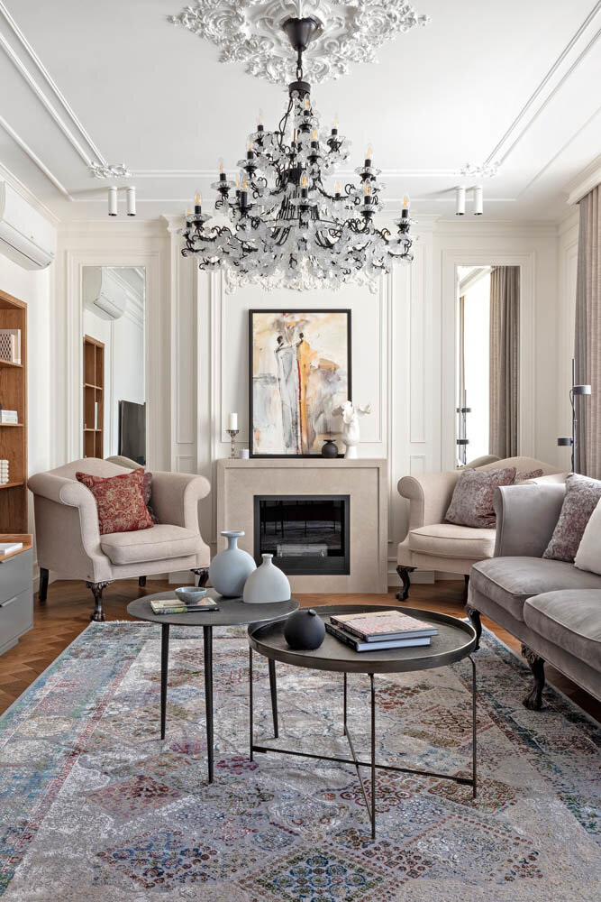 Композиционный центр в гостиной — биокамин с лаконичным мраморным порталом. Его очертания рифмуются со строгой рамкой из гипсовых молдингов на белой стене. Зеркальные панели по бокам от камина зрительно расширяют пространство комнаты. Абстрактная живописная работа в пастельных тонах на каминном портале создана казахстанской художницей Салимой Ширгалиевой. Обитая серым бархатом мягкая мебель в классическом стиле произведена белорусской компанией Furman. Авторы проекта: Яна Малыгина, Юлия Солнцева, Наталья Малыгина. Фото: Антон Петраков