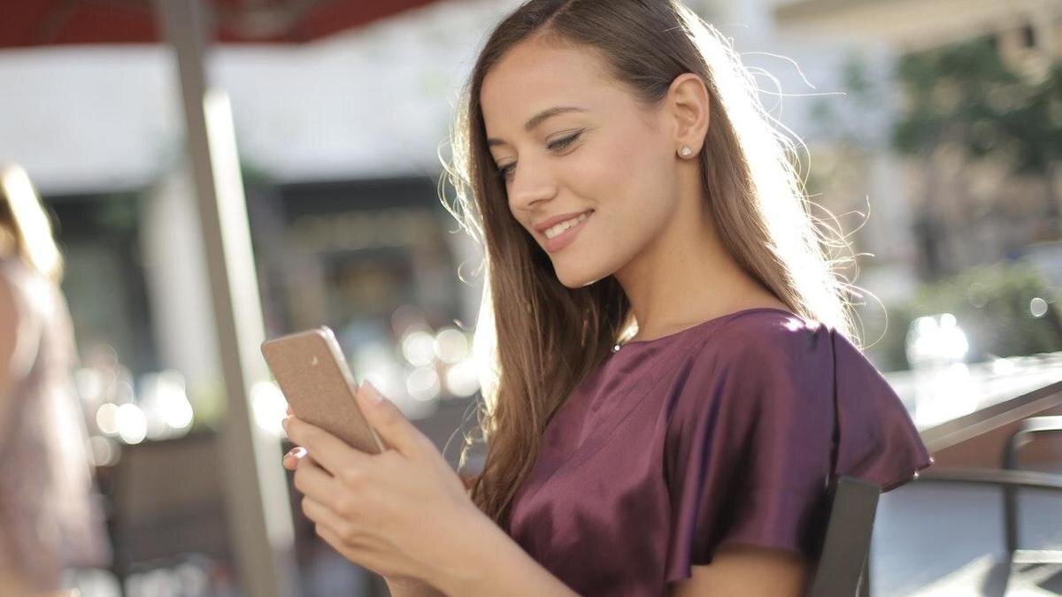    Девушка с телефоном улыбается, глядя на экра:Pexels