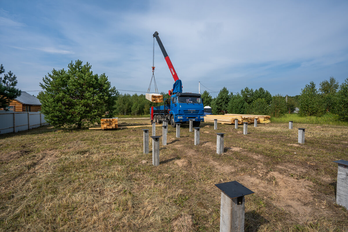 Вот так выглядит свайно-забивной фундамент. На фоне — разгрузка бруса. 