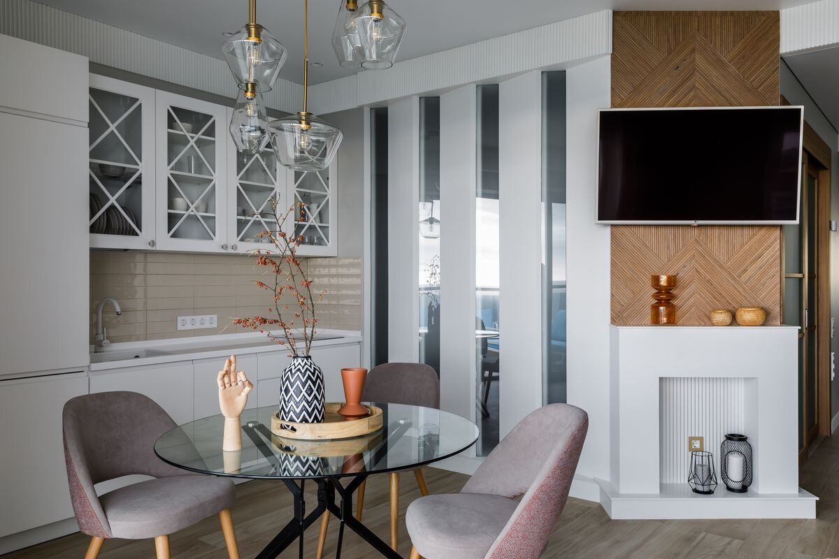 Скошенный угол спальни использовали, чтобы обустроить ТВ-зону. Под телевизором запланировали фальшкамин. Вертикальный рельеф портала перекликается со стеклянными вставками на смежной стене.