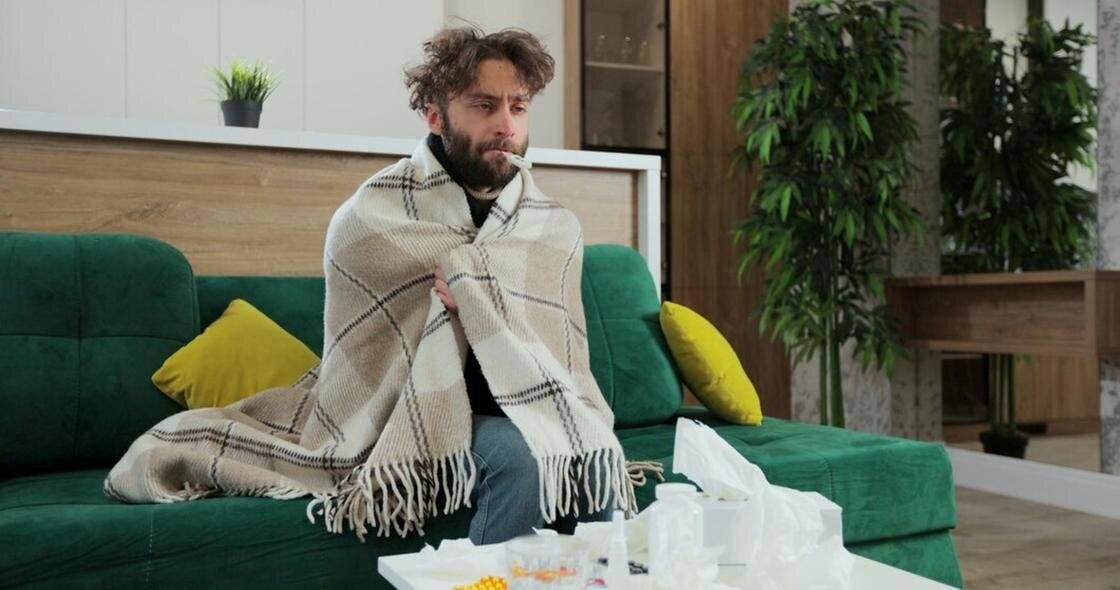    Больной мужчина сидит на диване, укутавшись в плед:Freepik
