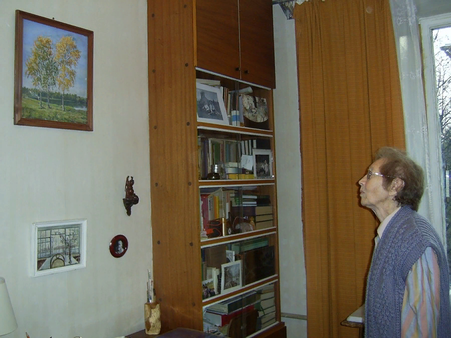 2012 г. В квартире дома по Университетскому проспекту в г. Москве. Елена Ильинична рассматривает картину «На озере» известного художника Игоря Эммануиловича Грабаря (1871 — 1960), которую он написал на даче в Косино под Москвой летом 1926 года.