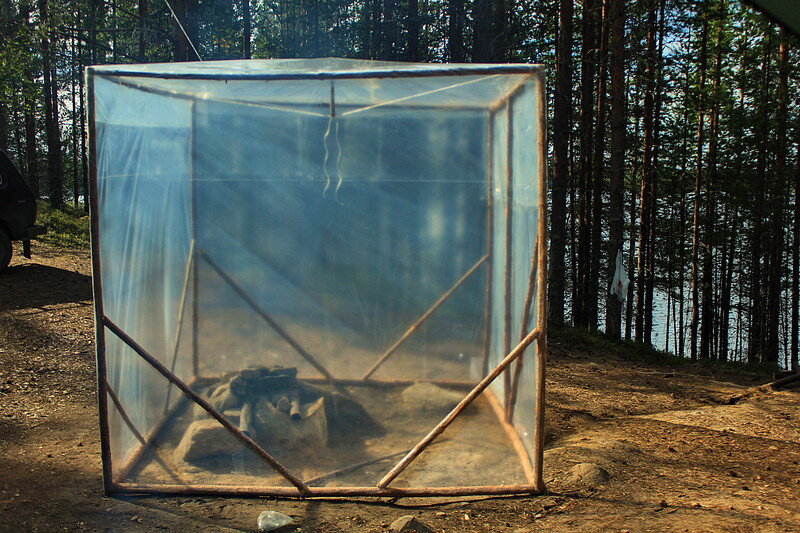 Вариант бани из пленки и разных палок, достаточно аккуратно сделан. Внутри очаг, сверху на камни положены куски труб, как основа, чтобы поставить емкость для нагрева воды