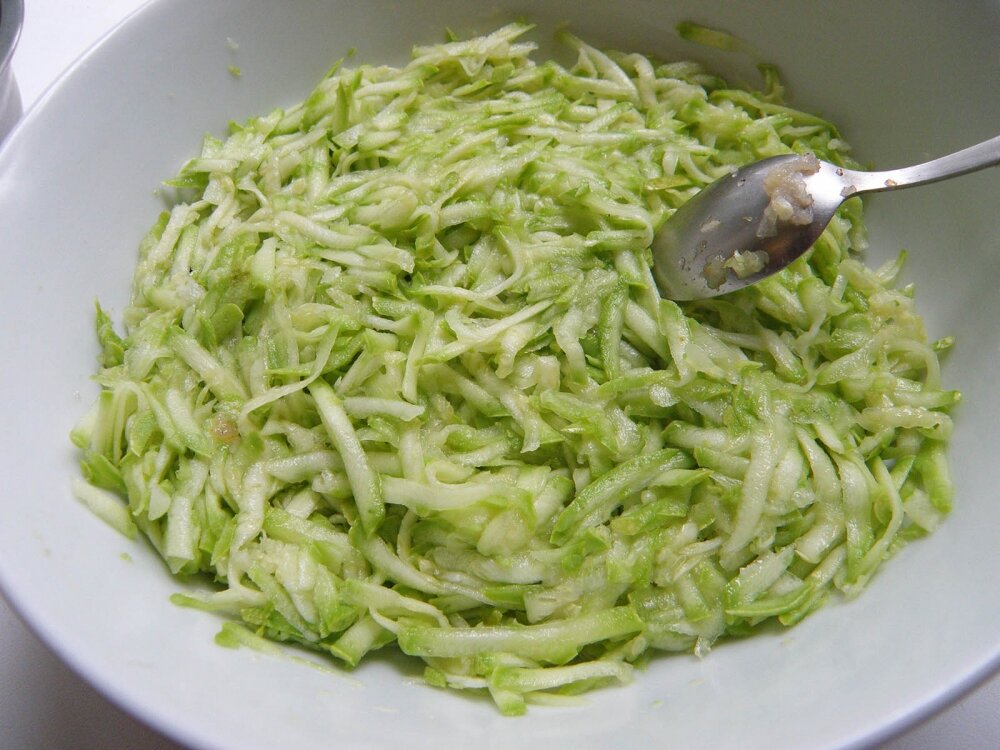 1. Сначала включим духовку, чтобы она нагрелась до 180 градусов, и отправим рис вариться. Чистые и без плодоножек кабачки измельчим на крупной терке. Чтобы кабачковые гнезда с фаршем не развалились при готовке, надо отцедить лишнюю жидкость. Для этого подсолим тертый кабачок, и отправим массу в миску минут на 10.