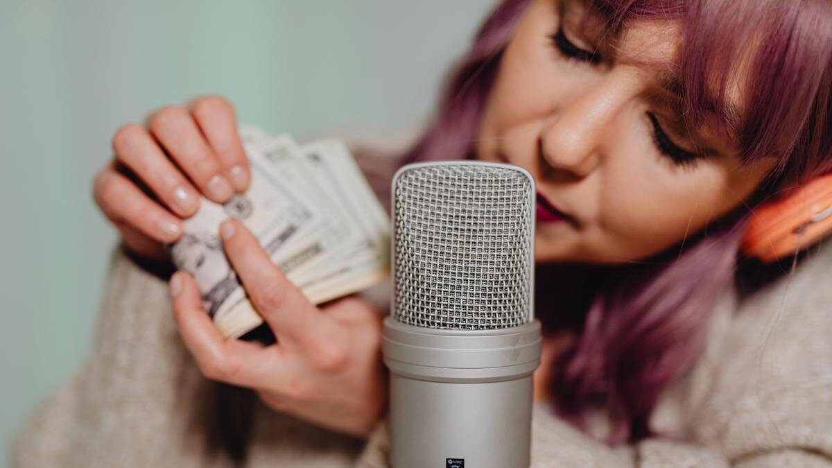    Девушка дует в микрофон и хрустит возле него новыми купюрами:Pexels