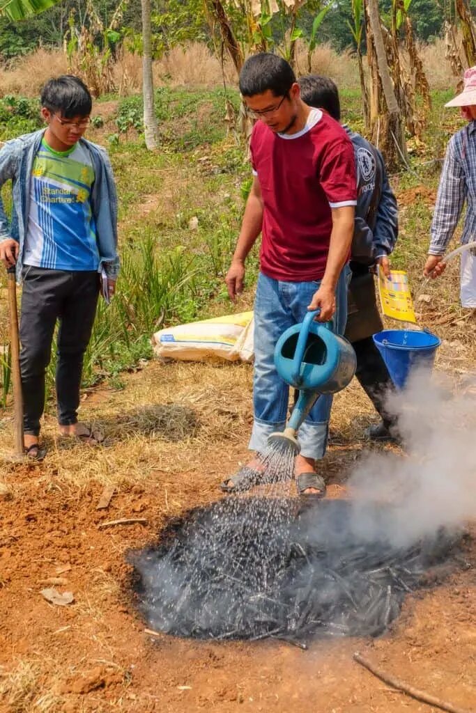 Тачилейк, Мьянма – 31 марта 2017 г. Тушение огня в яме для создания биоугля.