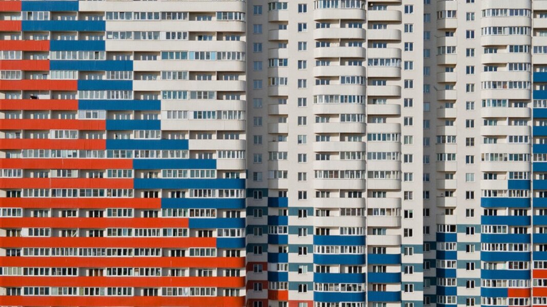 На снимке показан многоквартирный дом с фасадом, изображенным в цветах российского государственного флага в Санкт-Петербурге, Россия.