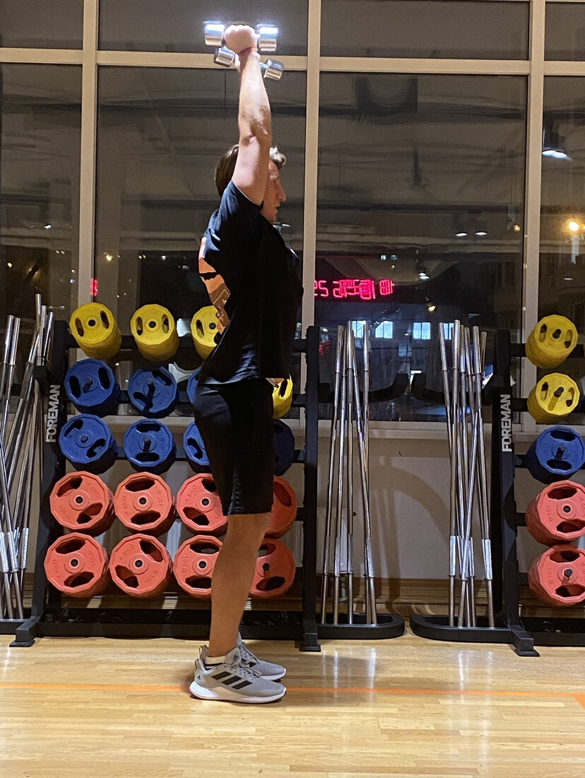 Встаньте прямо, возьмите в руки средний вес гантелей для соответствующий вашему уровню подготовки, можно на начальном уровне с маленьким весом, чтобы почувствовать мышцы трицепса. 
Поднимите гантели над головой, руки параллельно друг другу, не разводите их в стороны.