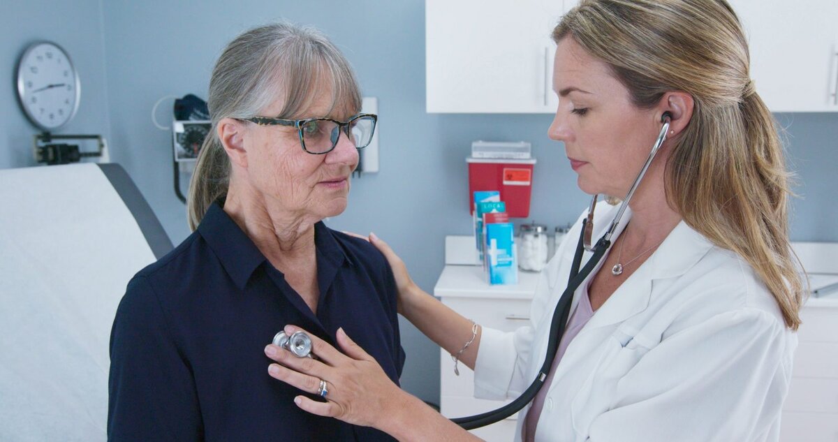    Female doctor using stethoscope listening to senior patients heart. Older woman visiting her primary care physician for a regular check up Редакция Calend.ru