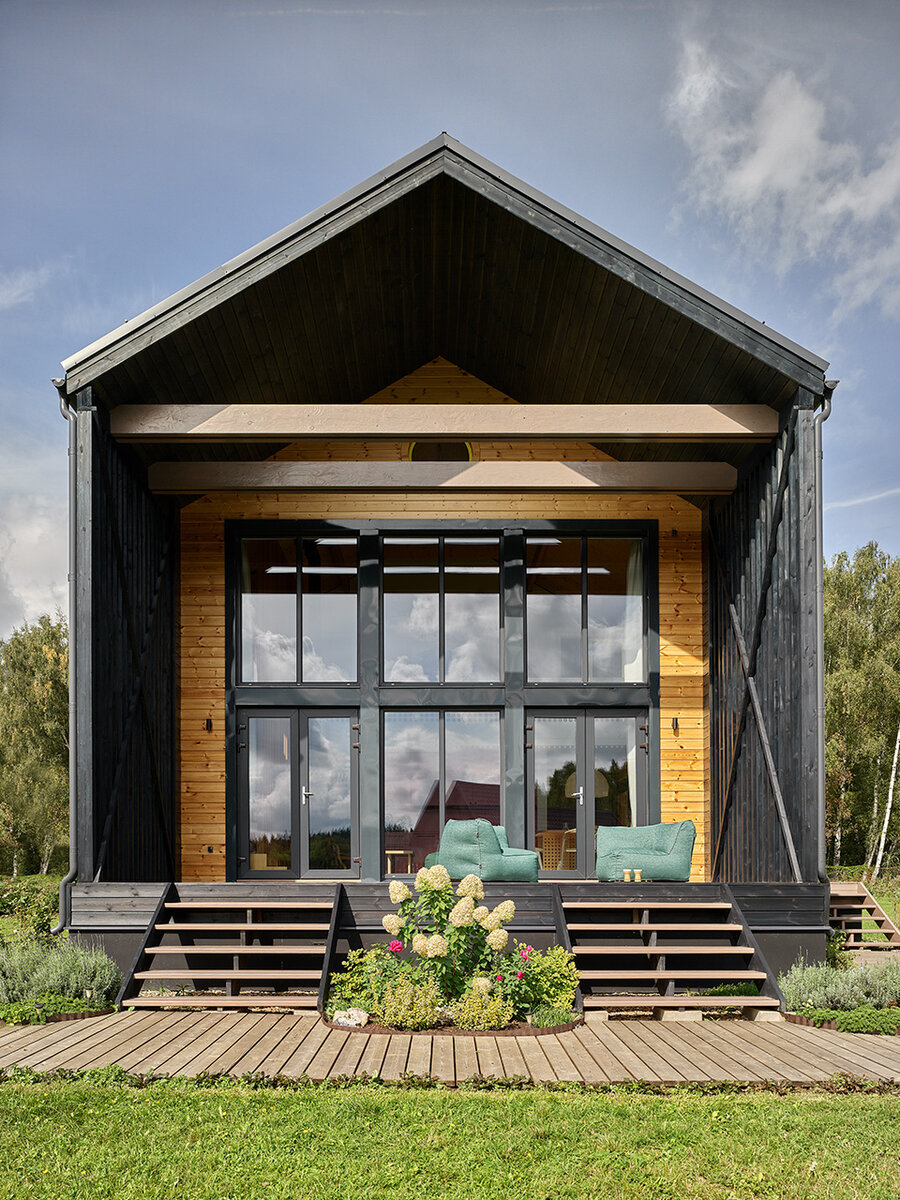 Веранда обращена на юго-восток. Кресла хозяева впервые вытащили на улицу во время съемки — и стали практиковать это регулярно, съемные чехлы позволяют. В раму остекленного фасада изнутри встроен экран домашнего кинотеатра, а кинопроектор находится в одном из кухонных шкафов.  