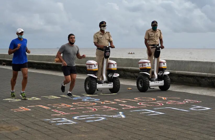 Police officers patrol on Segways as men wearing protective face masks run along the promenade at Marine Drive, after authorities eased lockdown restrictions that were imposed to slow the spread of the coronavirus disease (COVID-19)
