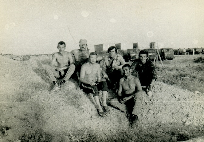 Вечерняя побывка на "Нептуне". Слева, за земляной насыпью, скрывается небольшой пруд, специально вырытый.  Позади сидящих (ближе к ним) видны четыре машины МАЗ-504 кандагарского Военторга, с контейнерами.
Ещё дальше - "отстойник" колонн, где как раз видны наливники воинской колонны, остановившейся в "Кишке" на ночёвку.