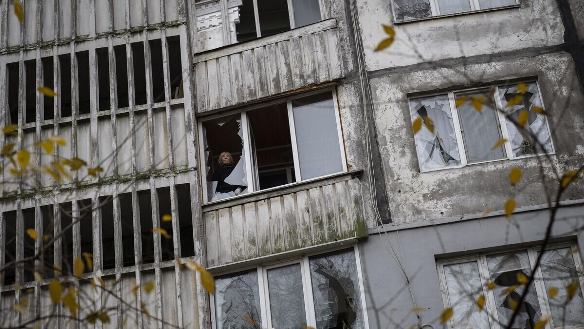    Женщина стоит около разбитого окна жилого дома в Херсоне© AP Photo / Bernat Armangue