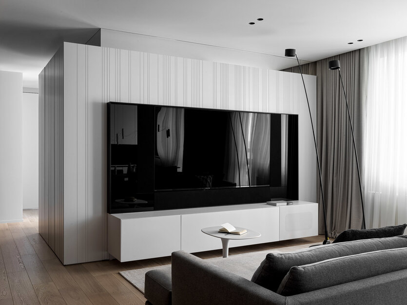 В зоне отдыха расположен белый куб — центральный геометрический объем, с одной стороны в него интегрирована система хранения, а с другой — зона ТВ, в которой телевизор сливается с плоскостью черного стекла. Архитекторы сделали специальную фрезеровку на фасадах, чтобы появилась текстура, а также постарались скрыть деление створок системы хранения. Диван Bristol, Poliform.