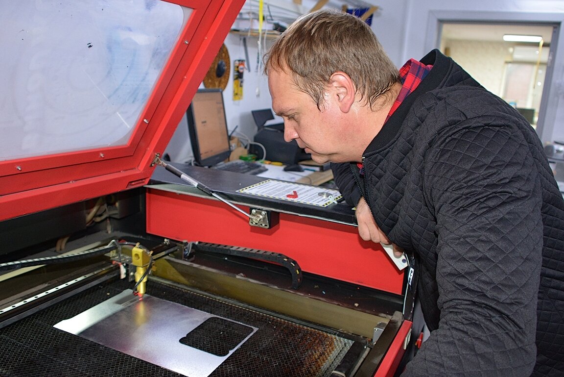 На компьютере Дмитрий Михнев задает задачу своему лазерному станку. Аппарат зажигается и начинает бегать по поверхности цветного пластика. Через пару минут мастер достает из станка готовый бейджик, который завтра украсит одежду персонала кафе или магазина. 