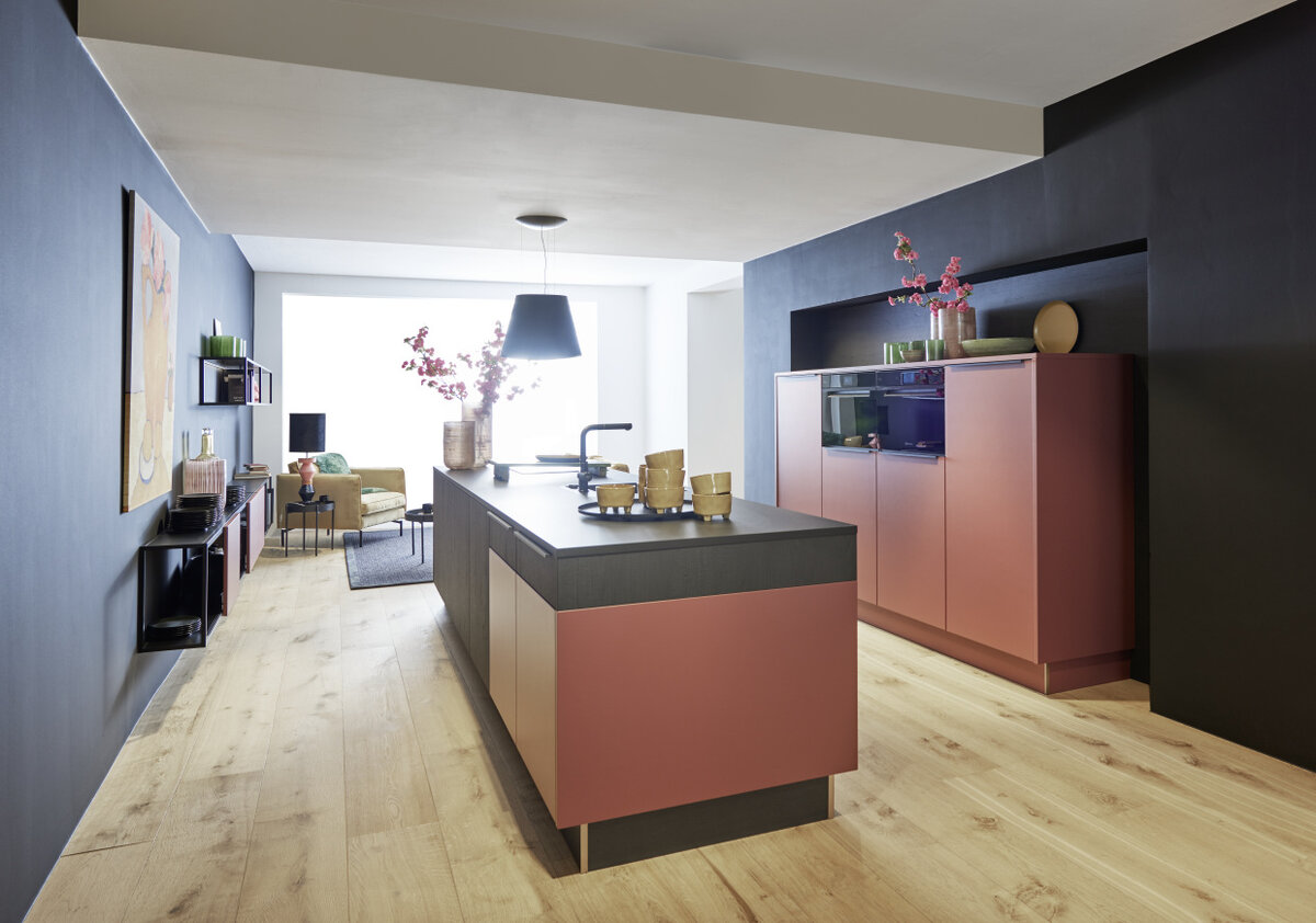 Фасады кухни Нольте, расположенные ближе к окну, верхняя часть и основание островного блока  изготовлены из шпона дуба программы Legno темного оттенка Eiche Sepia. Торцевая часть стола-острова выполнена в программе Soft Lack. Покрытие матовым лаком приглушенного красного цвета Hennarot перекликается с вертикальными колоннами