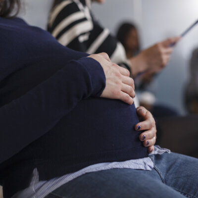    Close up of pregnant job recruiter holding hand on belly bump wainting in startup business office lobby area. Multi ethnic group of candidates reading cv resume before interview meeting Валерий