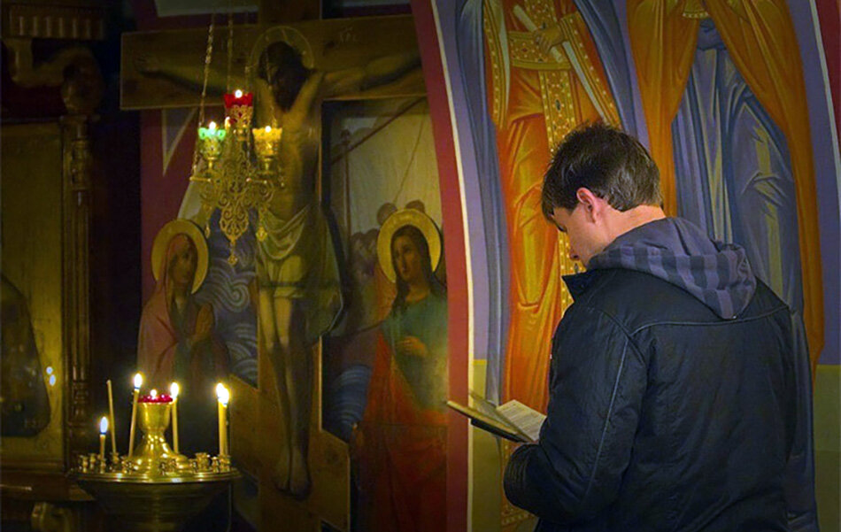 Мужчина ставит свечу. Мужчина молится в храме. Парень молится в церкви. Люди в храме. Человек перед иконой.