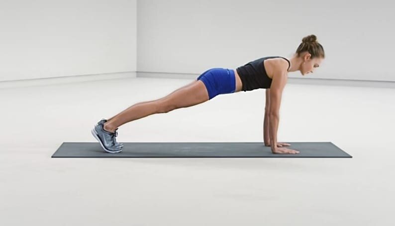 Расставь пальцы и упрись ладонями в пол. Плечи над кистями. Дави на стопы, чтобы задействовать ноги и ягодицы. Мышцы кора максимально напряжены. 