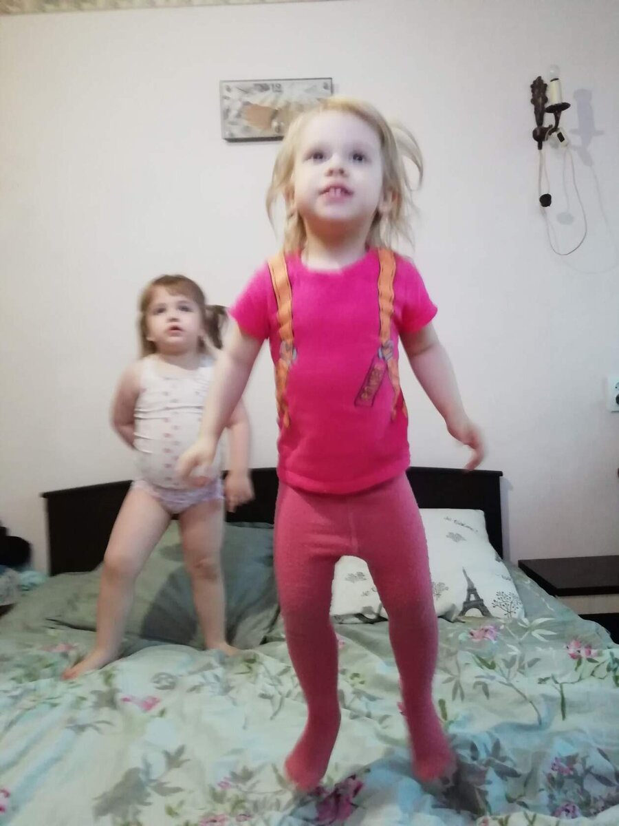 Полина прыгает на кровати родителей и смотрит мультики. На заднем плане фото Василиска-сладкоежка. Фото из домашнего архива. 2021 год