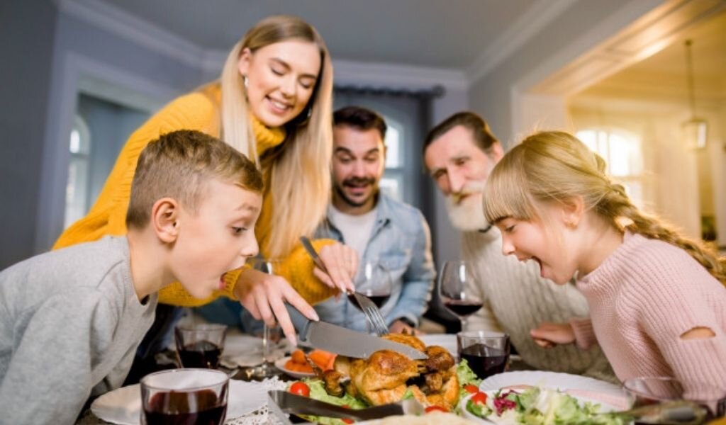 Праздничный семейный ужин. Источник фото: https://ru.freepik.com/premium-photo/thanksgiving-celebration-tradition-family-dinner-concept-funny-photo-of-big-family-sitting-at-the-table-mother-is-cutting-turkey-and-two-little-excited-children-looking-at-the-food_9140455.htm#&position=0